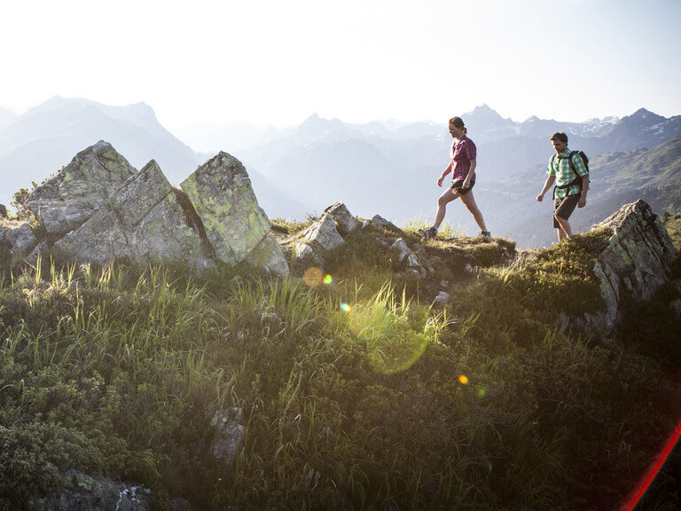 Zwei Wanderer wandern an auf einem Berg und genießen dabei ein wundervolles Bergpanorama.