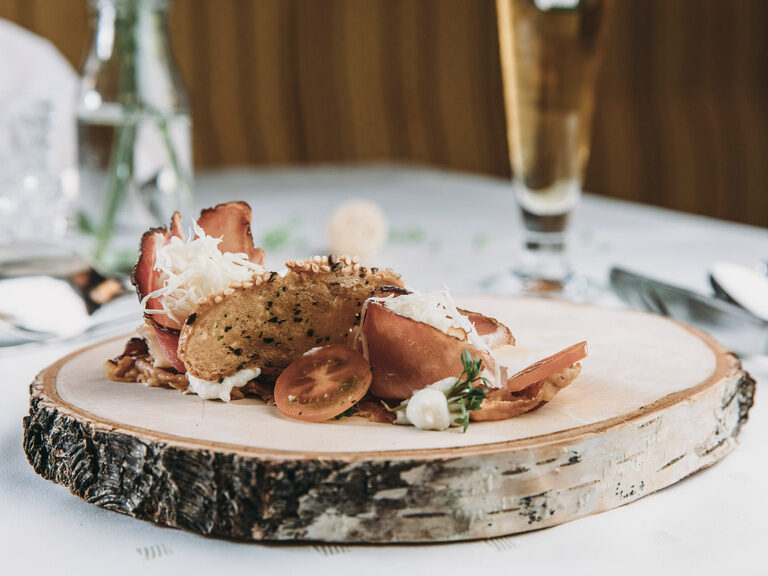 Auf einer Holzplatte als Teller ist eine Gericht kunstvoll drapiert.