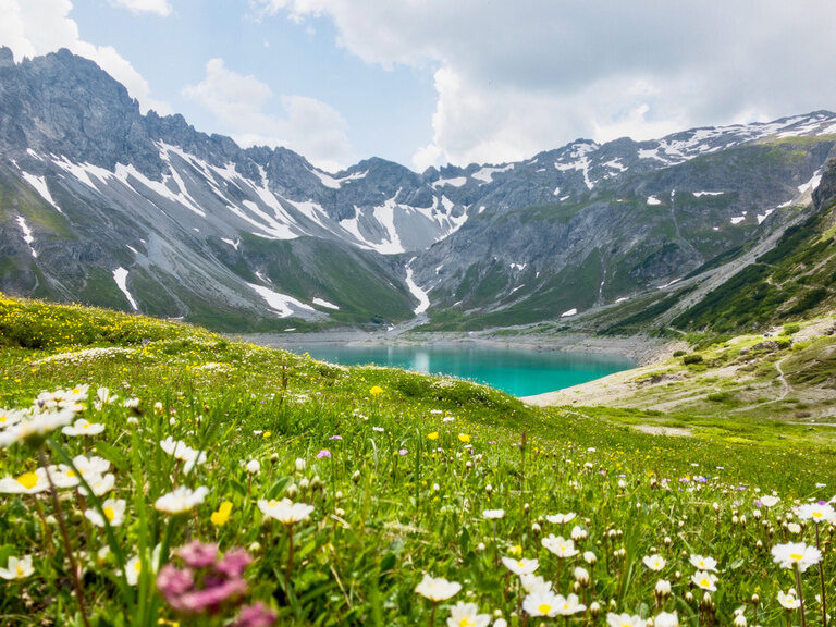Ein funkelnder Gebirgssee umgeben von saftigen Wiesen und einem beeindruckenden Bergpanorama in der Nähe von Montafon..